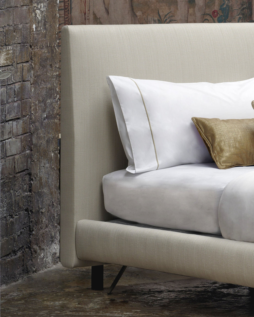 Beige sofa with white pillows and a gold pillow against a rustic wooden wall.