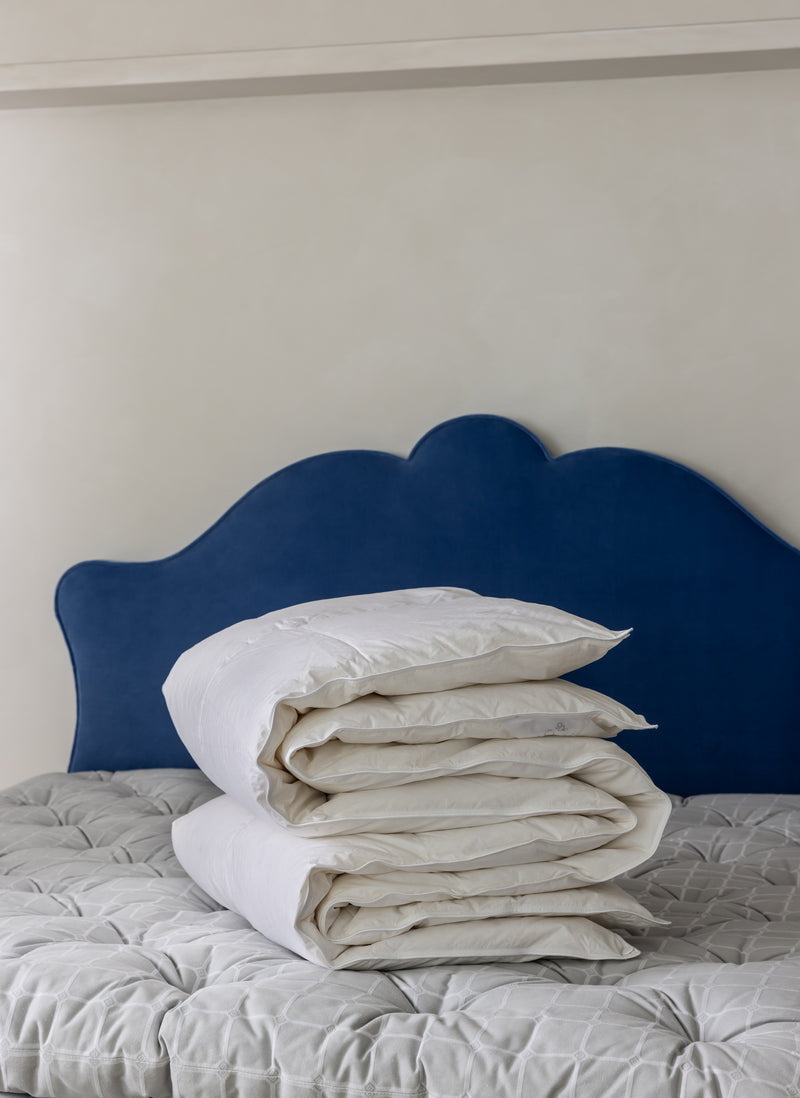 Folded Siberian duvet on a Savoir topper with a blue headboard.