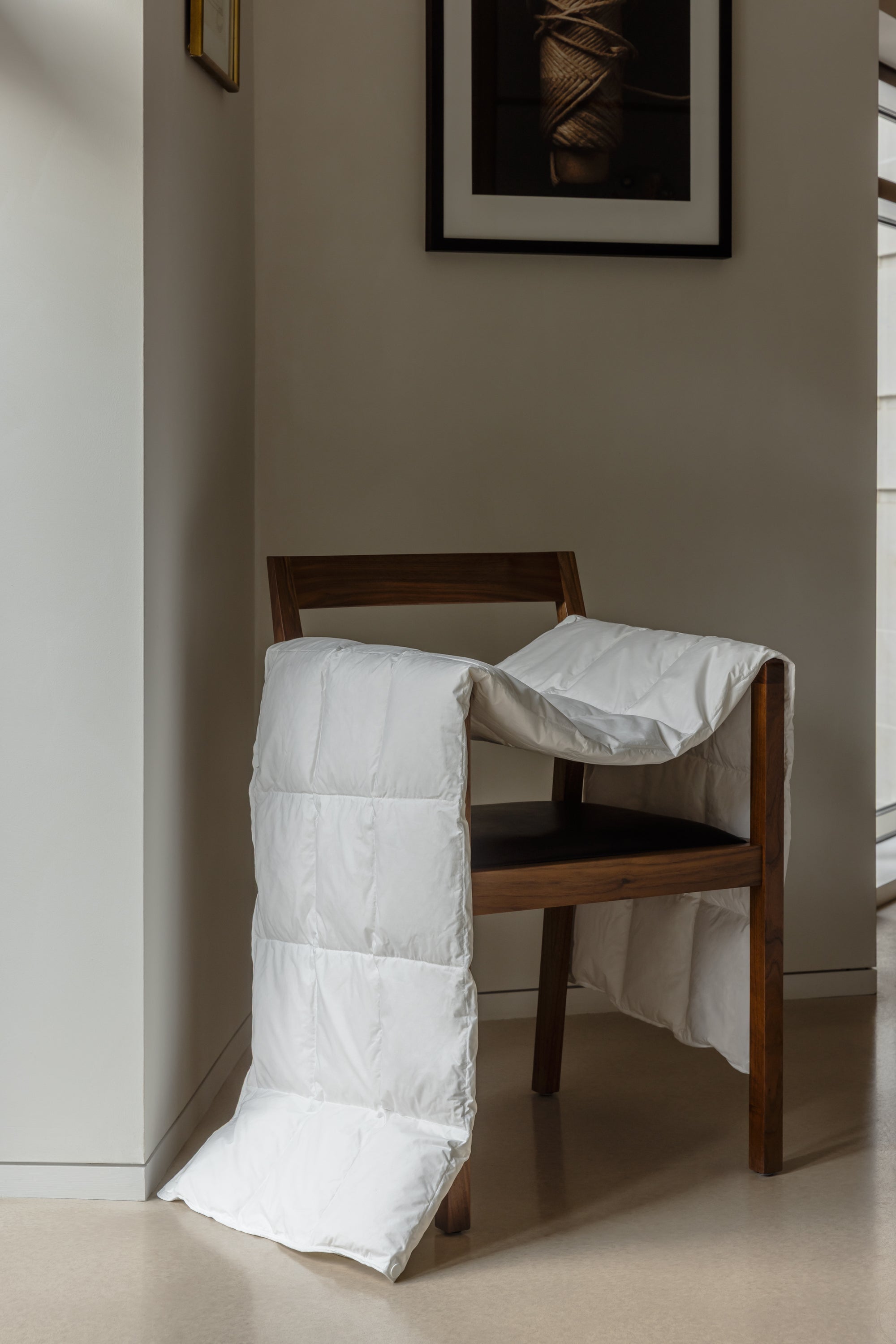 White comforter draped over a wooden chair against a neutral wall.