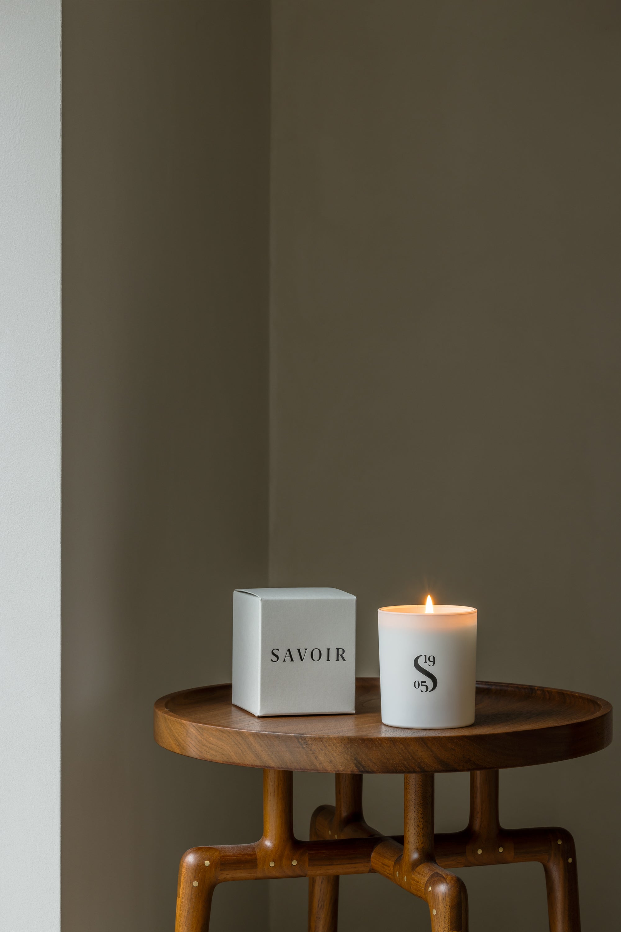 SAVOIR CANDLE LIT UP NEXT TO ITS BOX ON A WOODEN TABLE