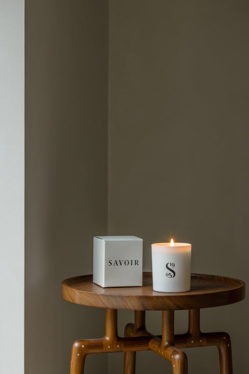 SAVOIR CANDLE LIT UP NEXT TO ITS BOX ON A WOODEN TABLE
