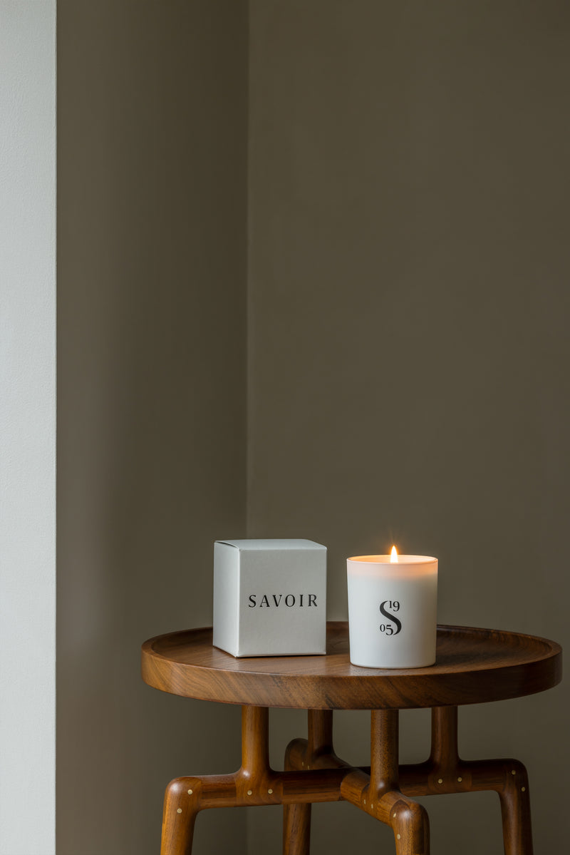 SAVOIR CANDLE LIT UP NEXT TO ITS BOX ON A WOODEN TABLE