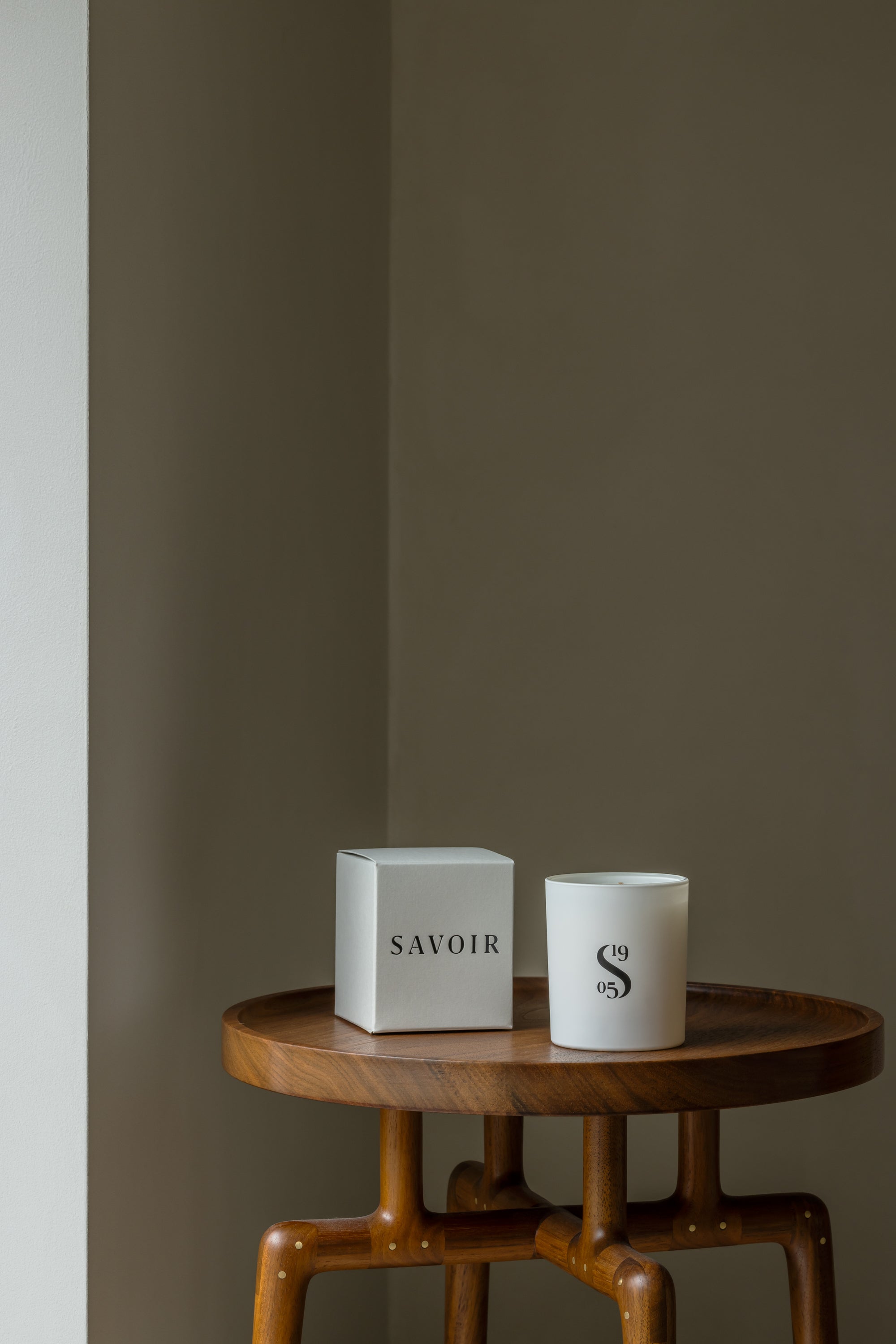 SAVOIR CANDLE UNLIT UP NEXT TO ITS BOX ON A WOODEN TABLE