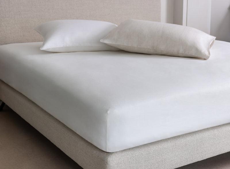 White fitted sheet on a Savoir bed with two pillows in a neutral room.
