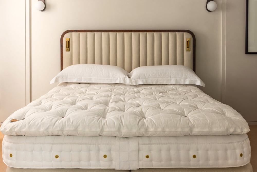 A whiter topper laid over a mattress on a bed, shown in a styled bedroom setting with the beige upholstered Luna headboard and two white pillows.