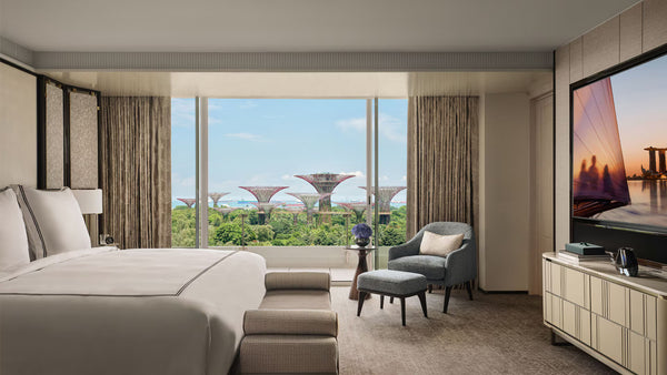 Modern suite bedroom at Marina Bay Sands Hotel with large windows, bed, chair, and TV, and stunning views of the outside
