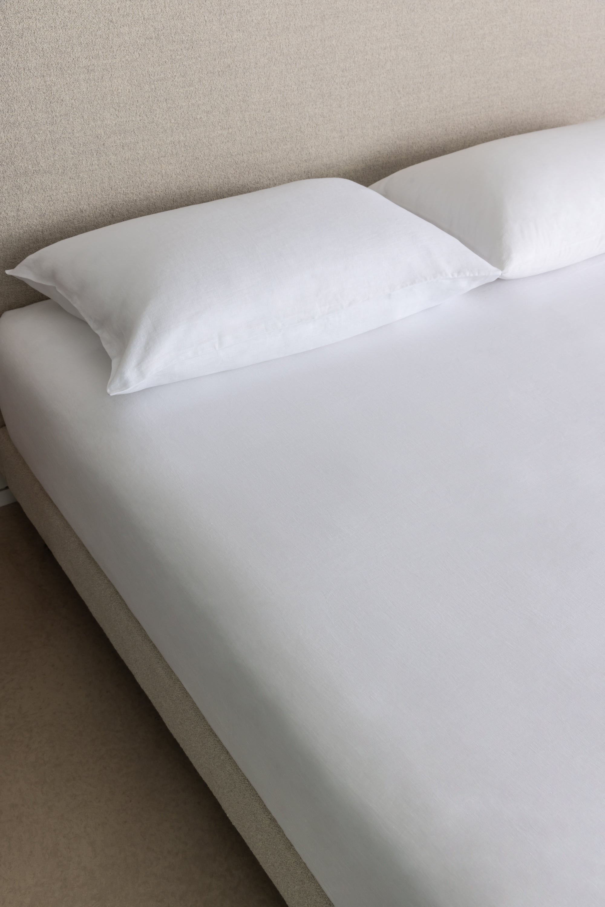 close up of organic linen fitted sheet on bed with two pillows