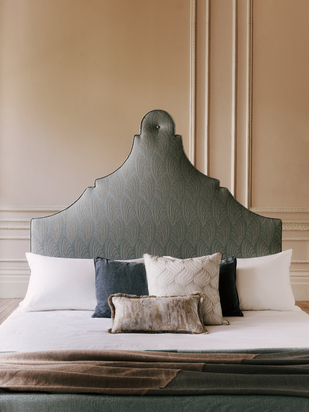 Light grey Claudia  headboard with patterned design and pillows against a beige wall.