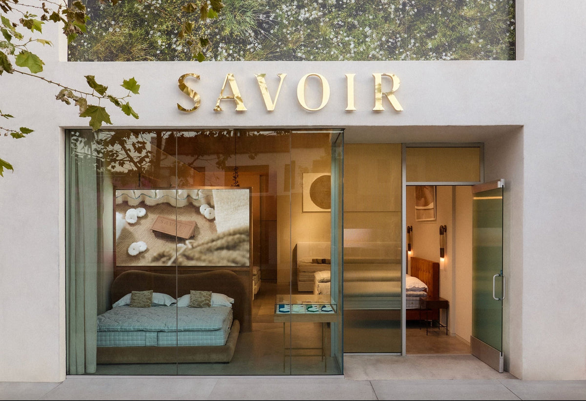 Savoir showroom store front with a large green forest-patterned wall mural and gold SAVOIR lettering above glass windows.