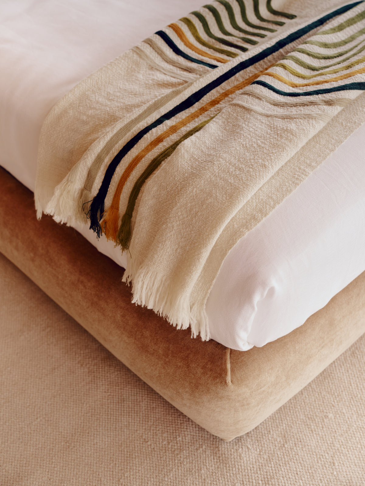 A close-up of a cream fringed throw blanket with forest green, olive green, and mustard yellow stripes on the brown upholstered Teddy bed base.
