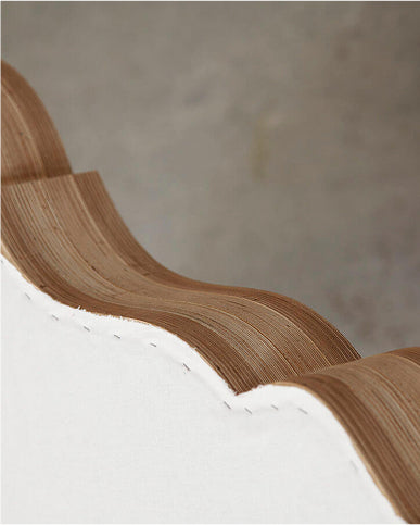 Close-up of a layered wooden trim  with visible wood grain and a white base, set against a neutral gray background.